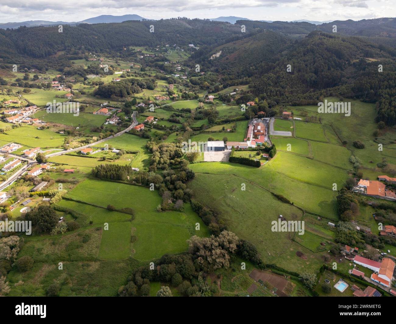 Un drone cattura la tranquilla bellezza di una verde area rurale con campi sportivi tra colline ondulate ed edifici sparsi. Foto Stock