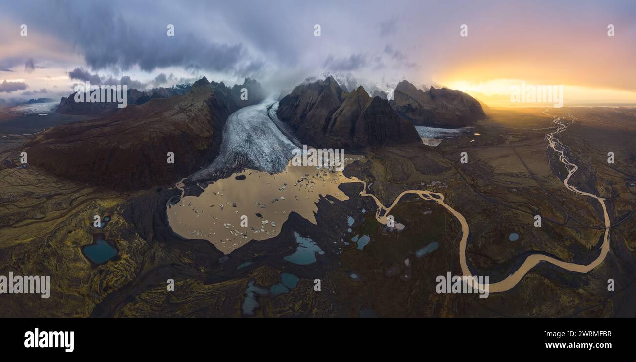 Scatto aereo panoramico mozzafiato che cattura il vasto ghiacciaio Vatnajokull davanti a un tramonto spettacolare, con tortuosi fiumi e l'aspra terra islandese Foto Stock