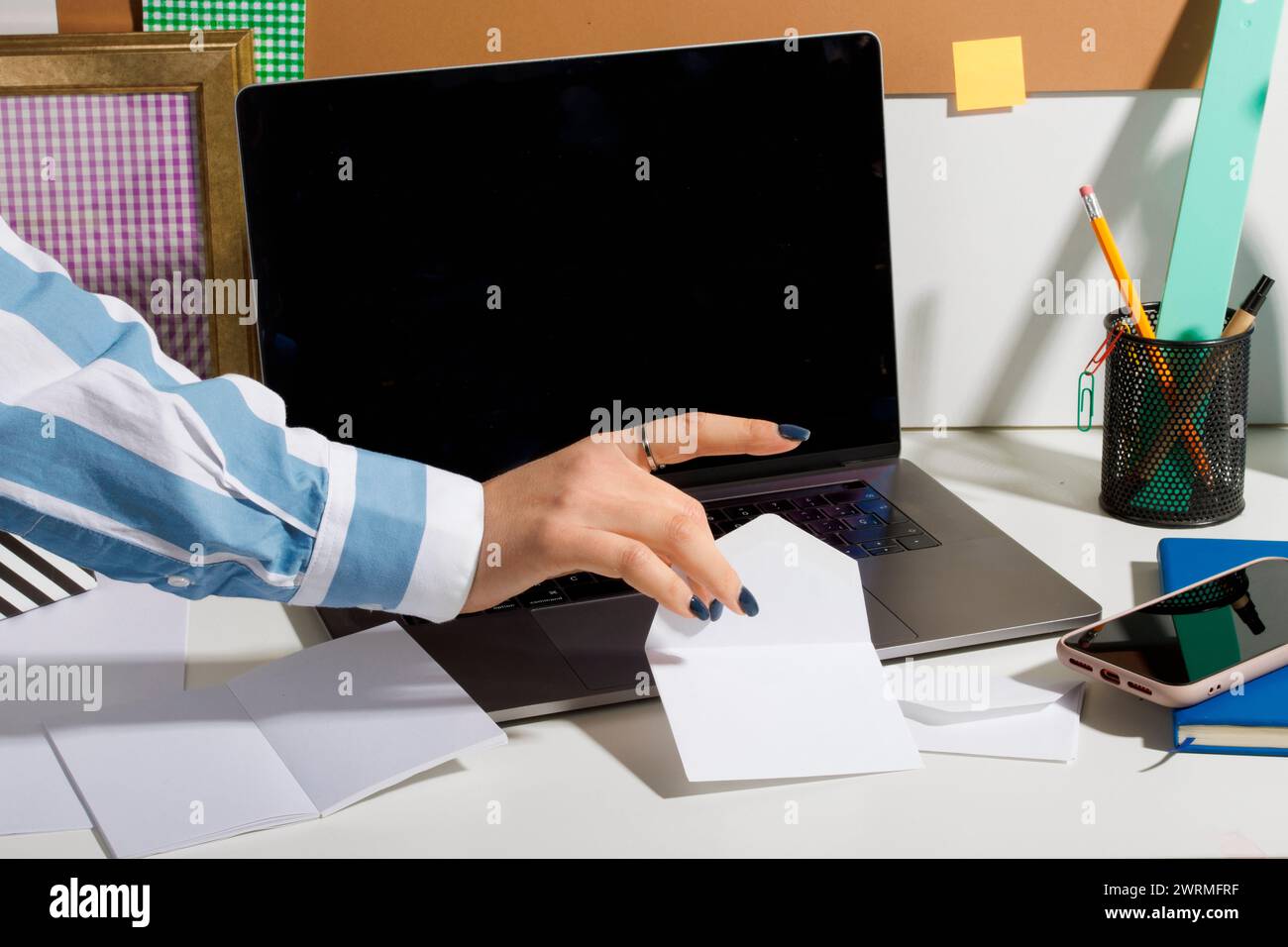 lavoratrice in ufficio corta e irriconoscibile che afferra una nota accanto a un notebook su una scrivania ben organizzata con varie forniture per ufficio. Foto Stock