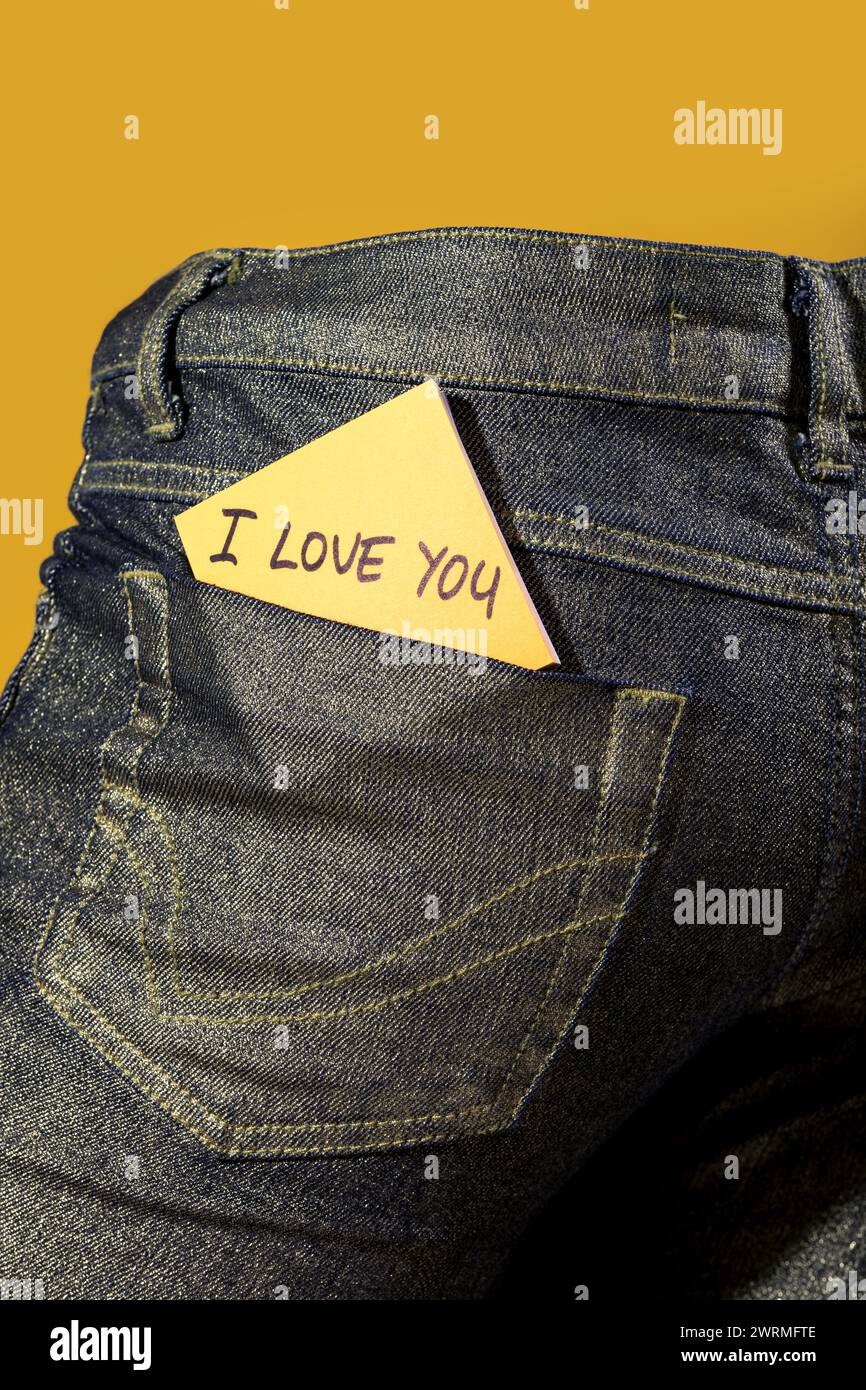 Una nota d'amore sentita su una carta adesiva gialla è sottilmente infilata nella tasca posteriore di un jeans su sfondo giallo Foto Stock