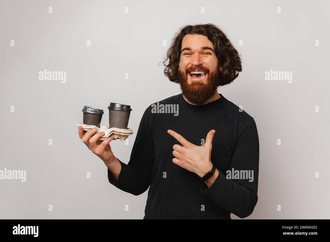 Bell'uomo barbuto con lunghi punti di capelli alle due tazze di carta da asporto che sta tenendo. Foto Stock