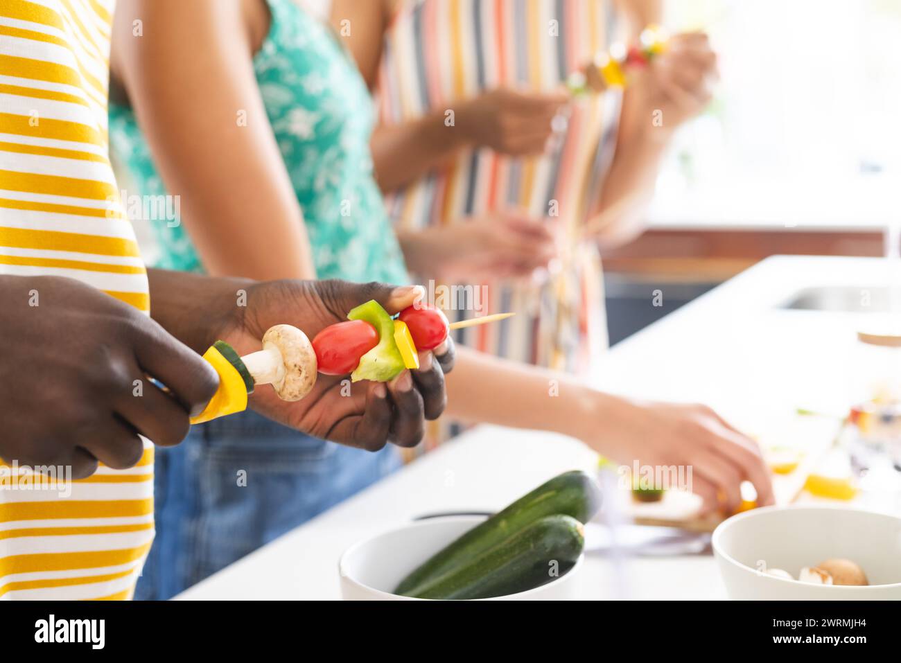 Gruppi diversi di persone che preparano spiedini di verdure in una cucina luminosa Foto Stock