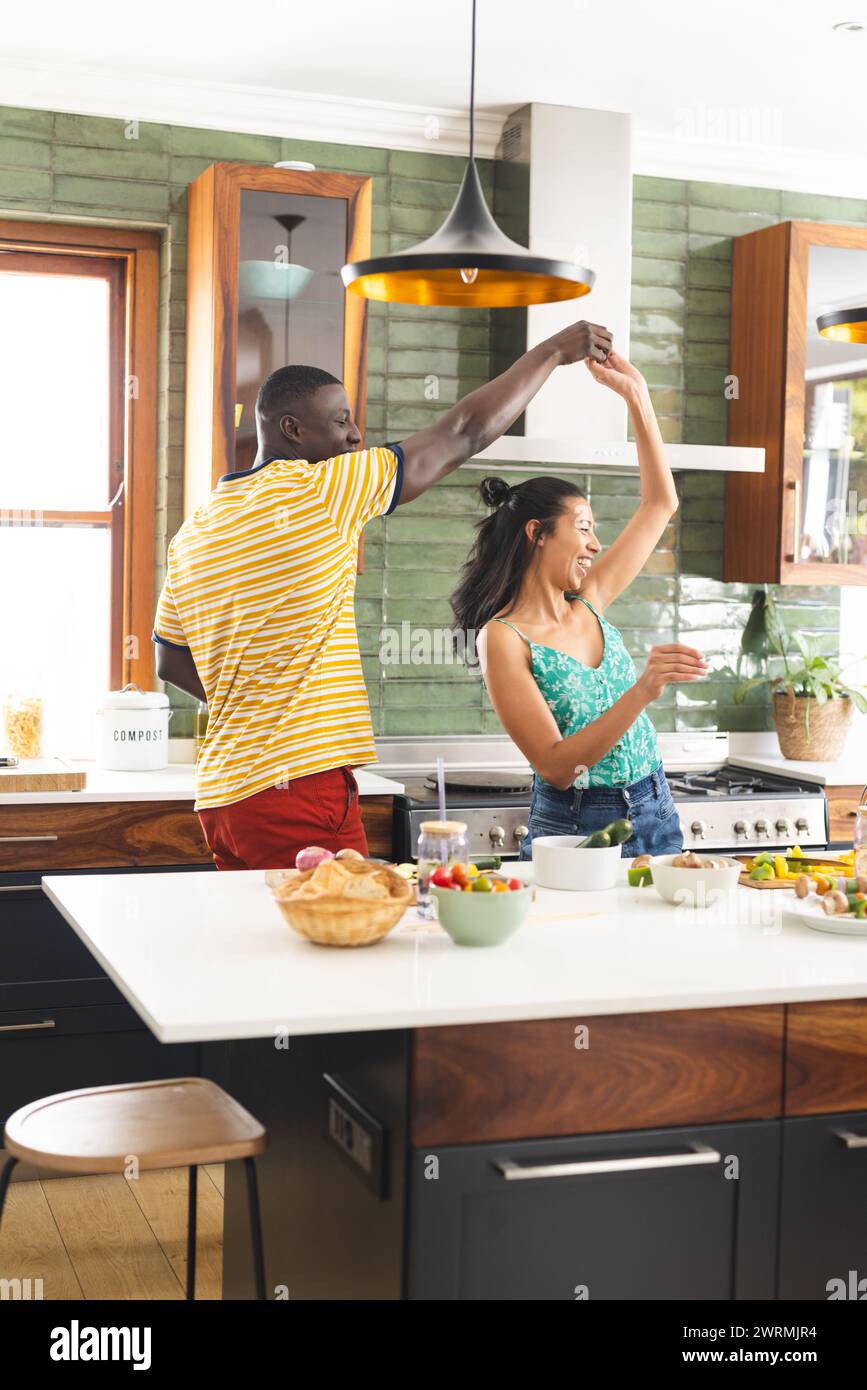 Il giovane afroamericano e la donna birazziale ballano gioiosamente in una cucina illuminata dal sole Foto Stock