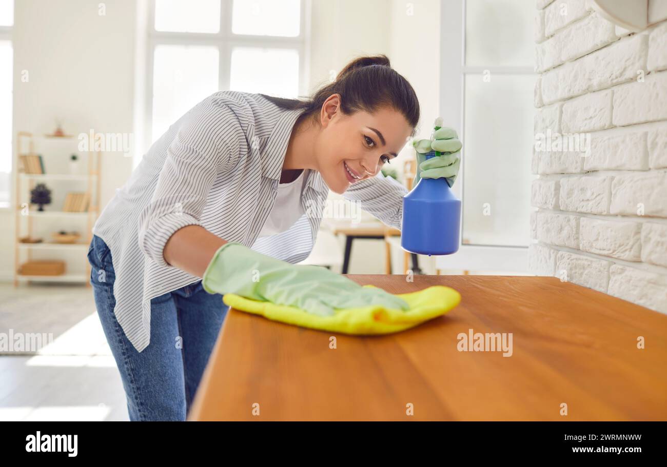 Felice giovane donna sorridente casalinga pulizia superficie del bancone in cucina con detergente. Foto Stock