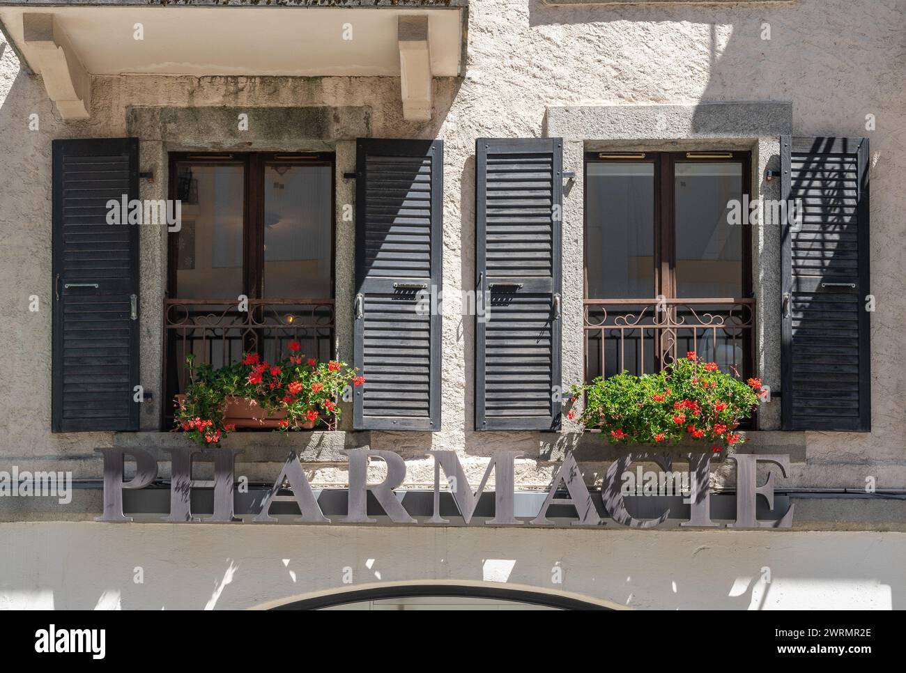 Facciata di un vecchio edificio con il segno metallico di una farmacia sotto un paio di finestre con gerani in fiore, Chamonix, Haute Savoie, Francia Foto Stock