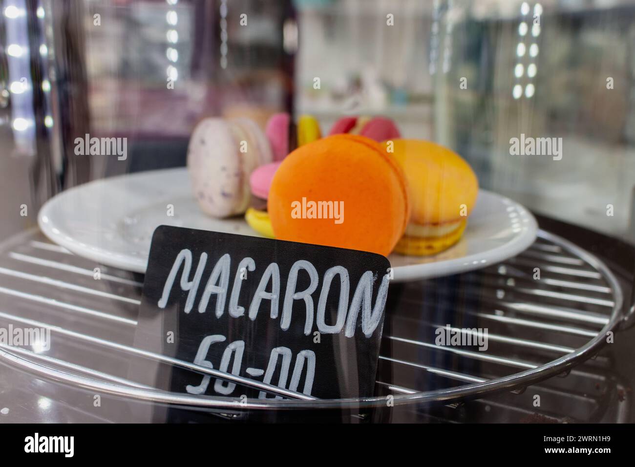 Macaron in mostra al bar. Torta di macaron con cartellino del prezzo. Concetto di cibo dolce. Dessert mattutino. Macaron d'arancia sul piatto sul mercato. Foto Stock