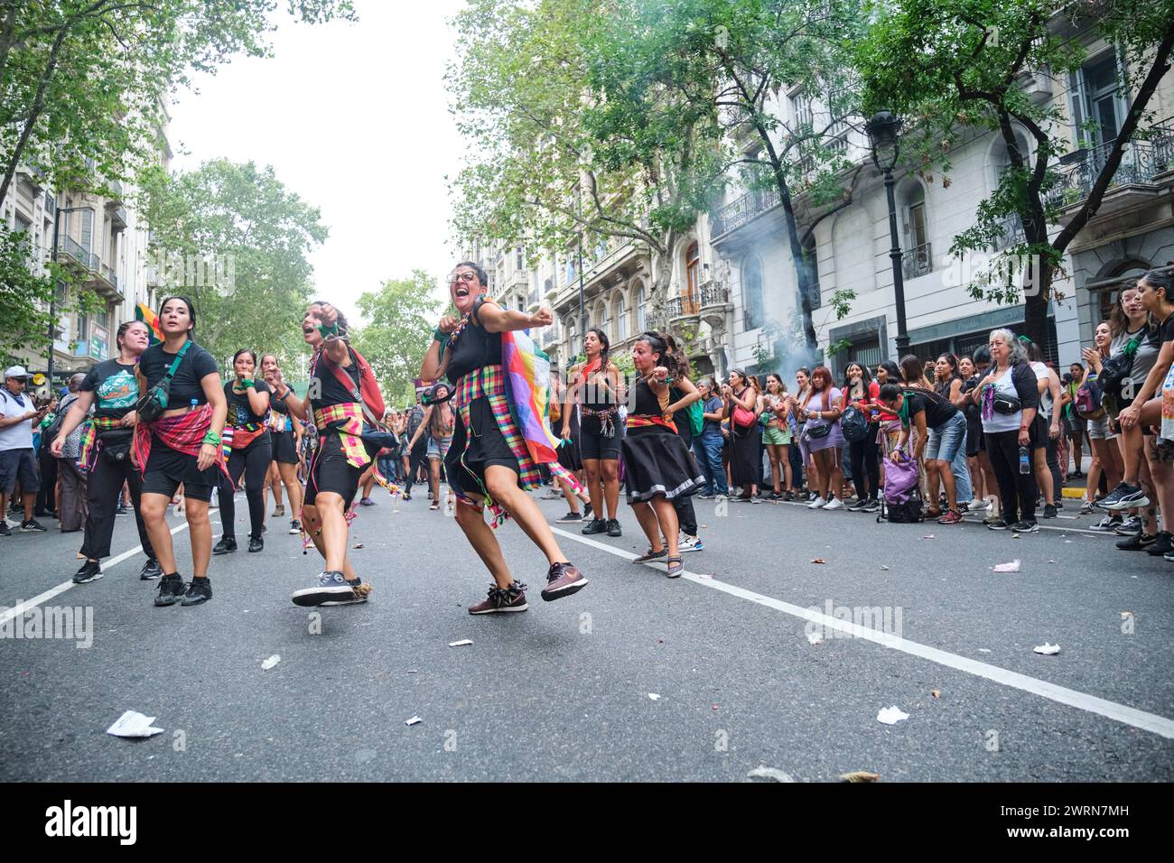 Buenos Aires, Argentina; 8 marzo 2024: Gruppo di donne che indossano tessuti tradizionali colorati e salutano la wiphala danzando durante la marcia Foto Stock