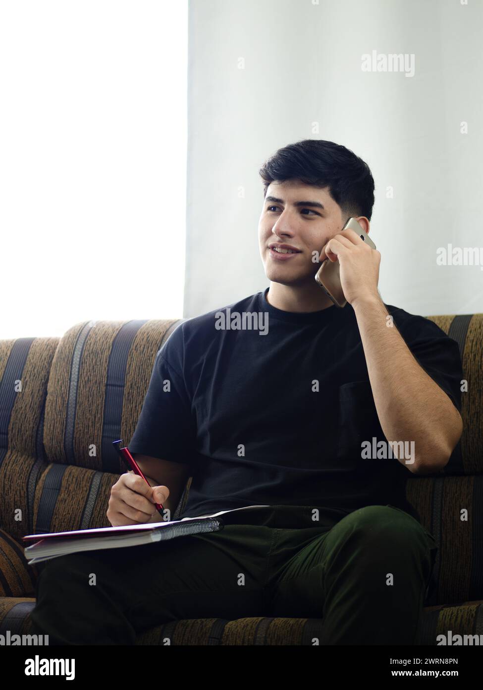 Immagine verticale di un giovane uomo che conduce affari telefonicamente, prende ordini o come contabile organizza e pianifica strategie Foto Stock