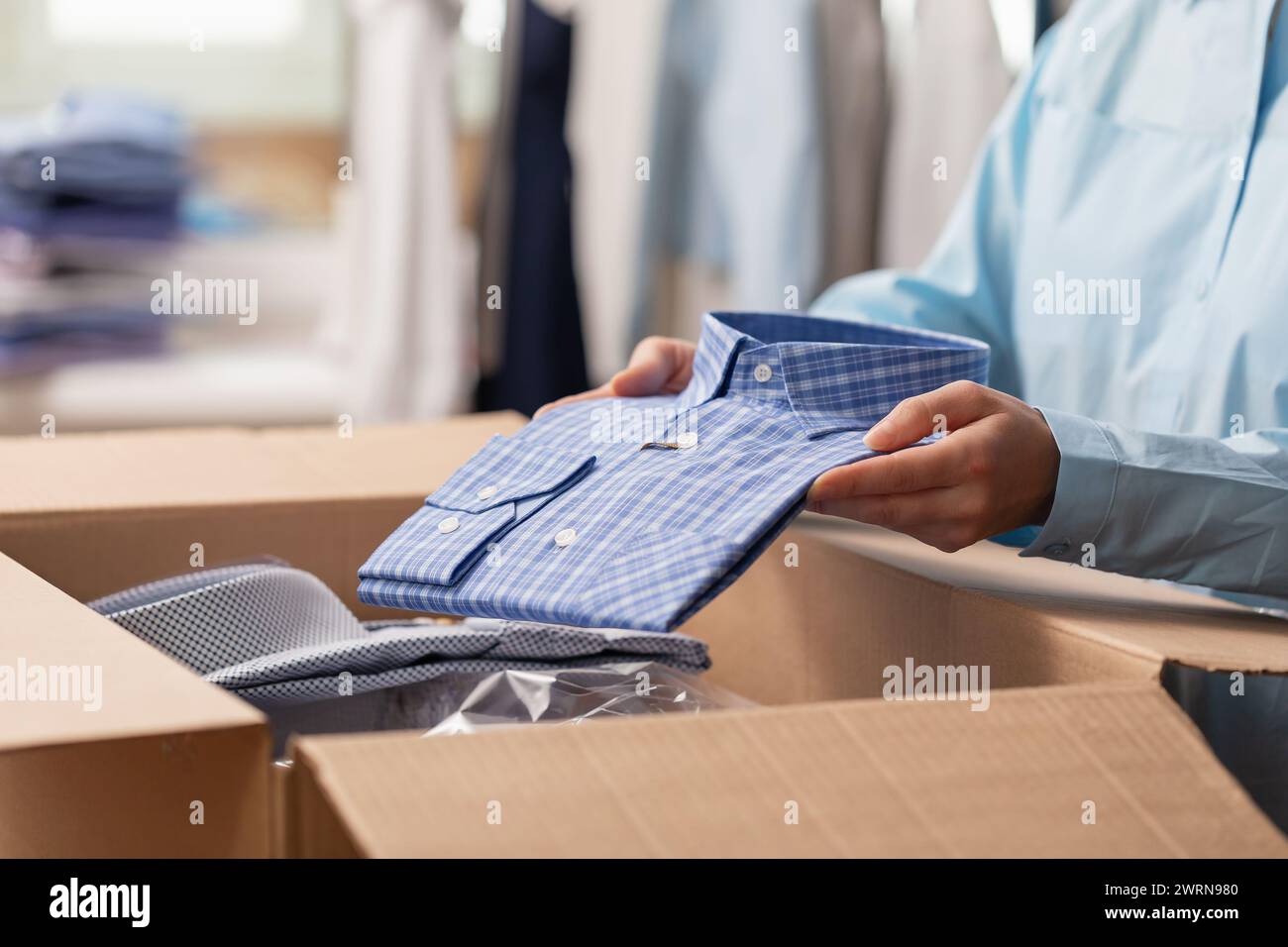 Un venditore mette una camicia piegata in una scatola per inviarla a un cliente, una donna invia la merce ai mercati Foto Stock