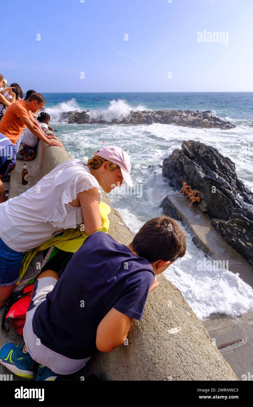 Manarola, IT - 25 luglio 2023: Persone che guardano grandi onde che si infrangono sulle rocce Foto Stock