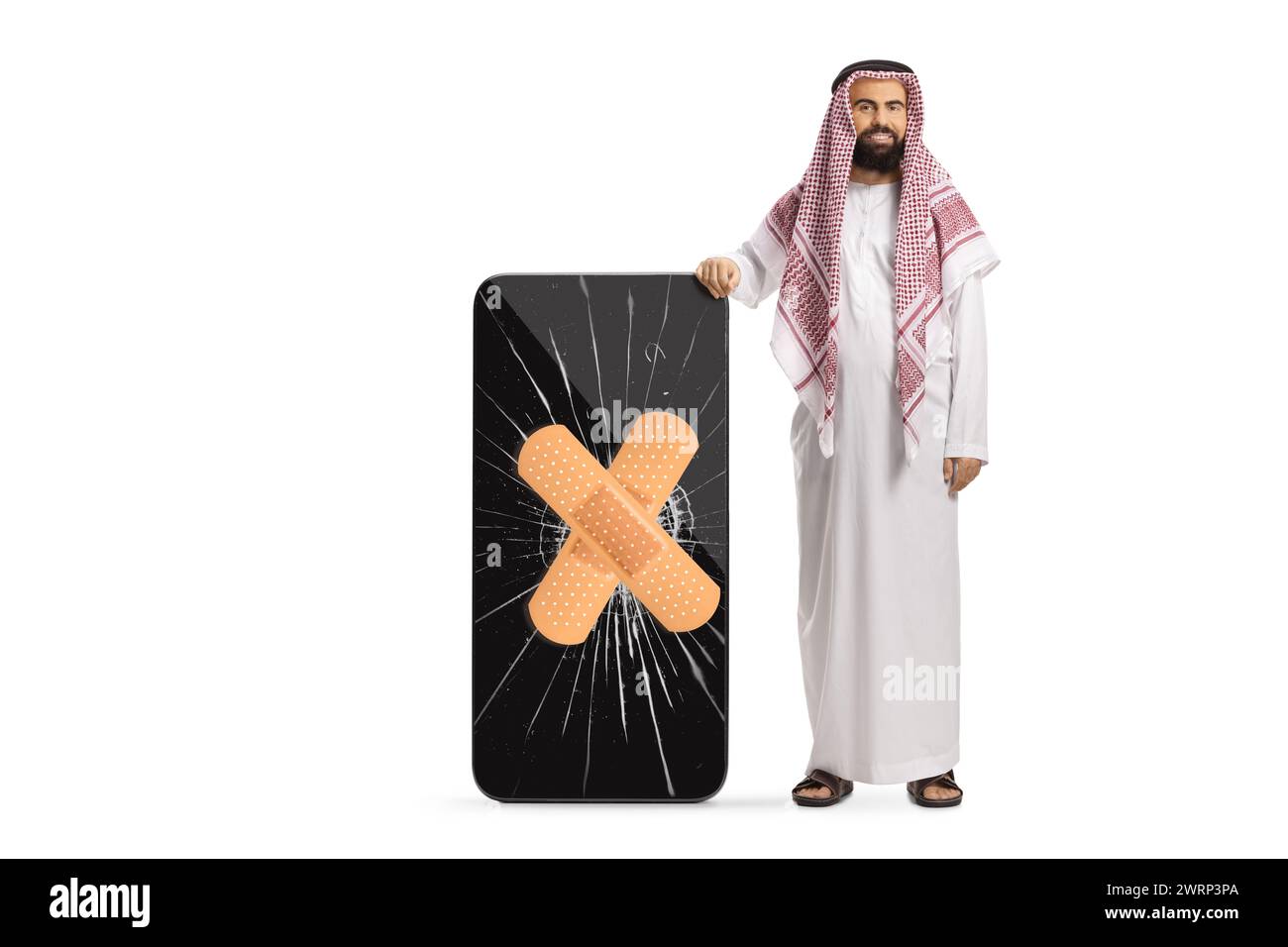 Uomo arabo saudita in abiti etnici in piedi accanto a un telefono cellulare con schermo incrinato isolato su sfondo bianco Foto Stock