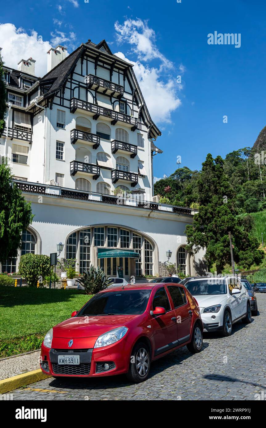 Vista parziale del Quitandinha Palace, un ex hotel storico con alcune auto parcheggiate nelle vicinanze in fila singola sotto il cielo nuvoloso del pomeriggio d'estate. Foto Stock