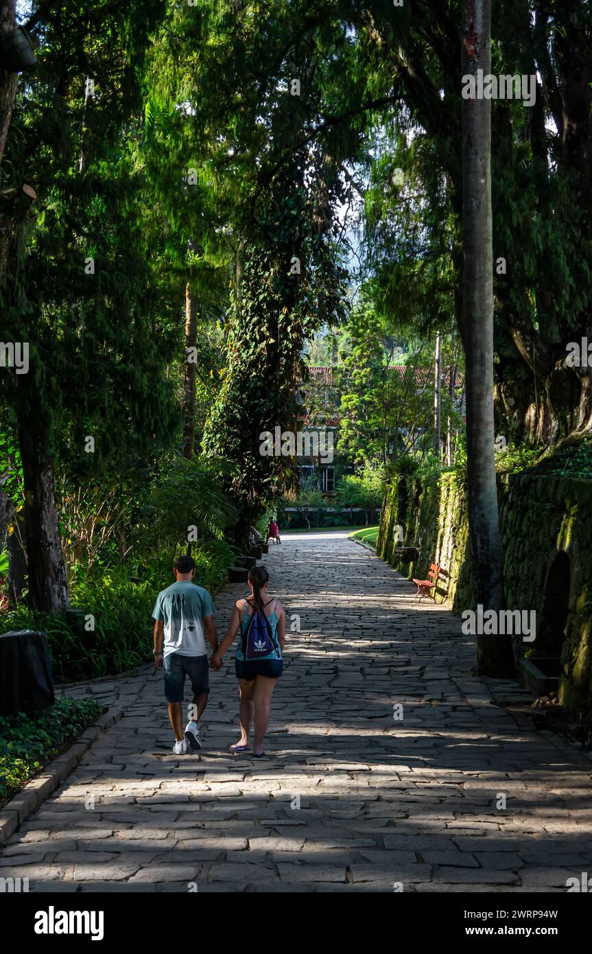 Una coppia cammina su uno dei sentieri dei giardini del Palazzo Imperiale di Petropolis nel quartiere Centro sotto il cielo azzurro nuvoloso del pomeriggio estivo. Foto Stock