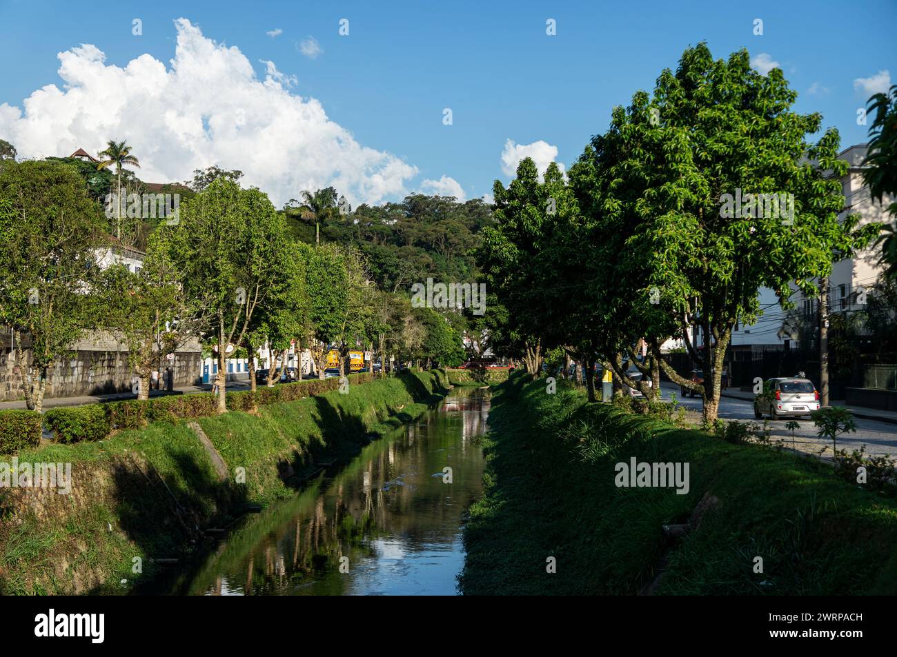 Vista del canale d'acqua del fiume Piabanha che scorre tra Tiradentes avenue nel quartiere Centro sotto il cielo nuvoloso soleggiato del pomeriggio estivo. Foto Stock