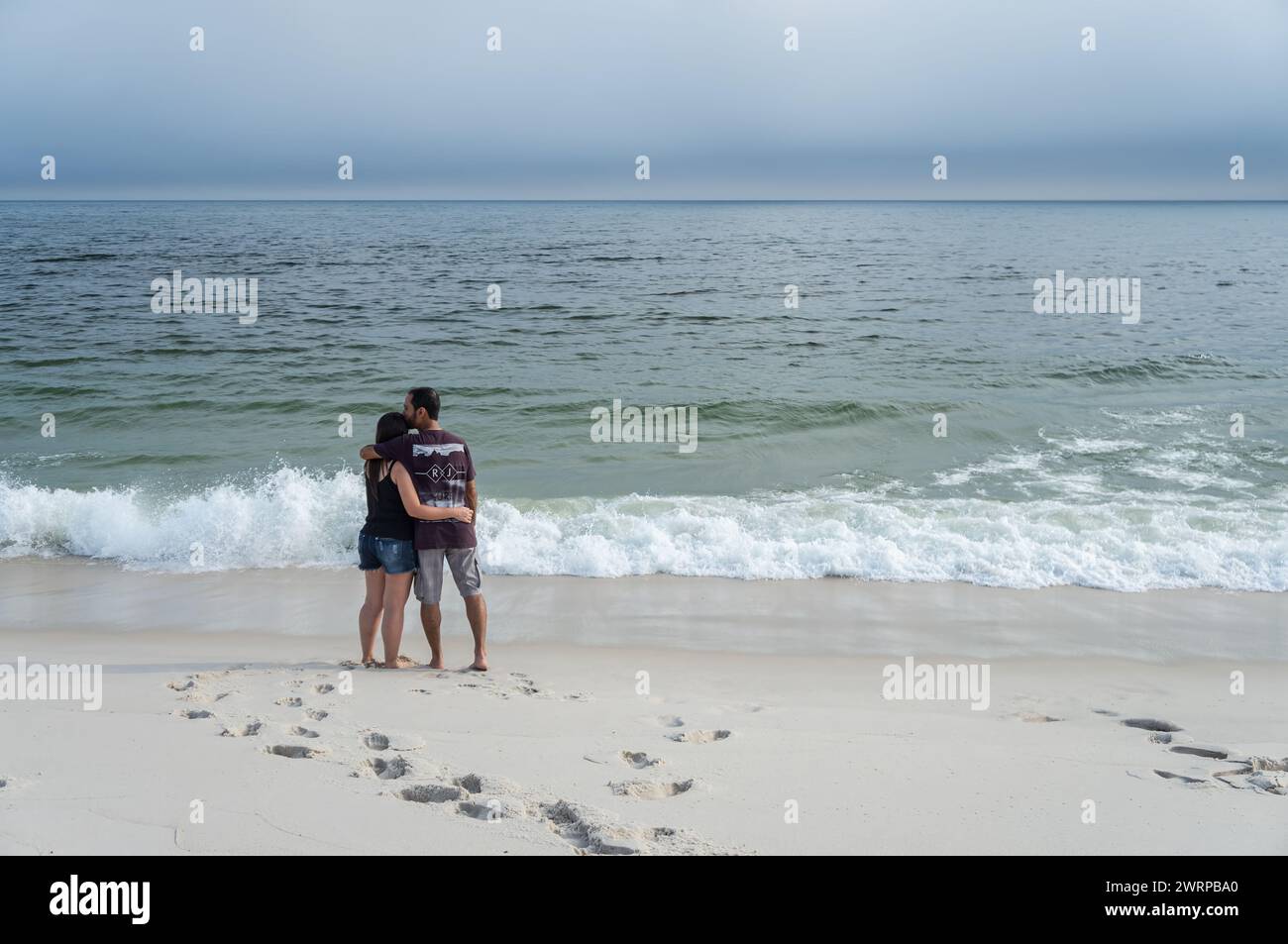 Una coppia innamorata che si abbraccia sulle sabbie bianche della spiaggia di Praia Seca e guarda le acque dell'Oceano Atlantico sotto il cielo nuvoloso del pomeriggio d'estate. Foto Stock