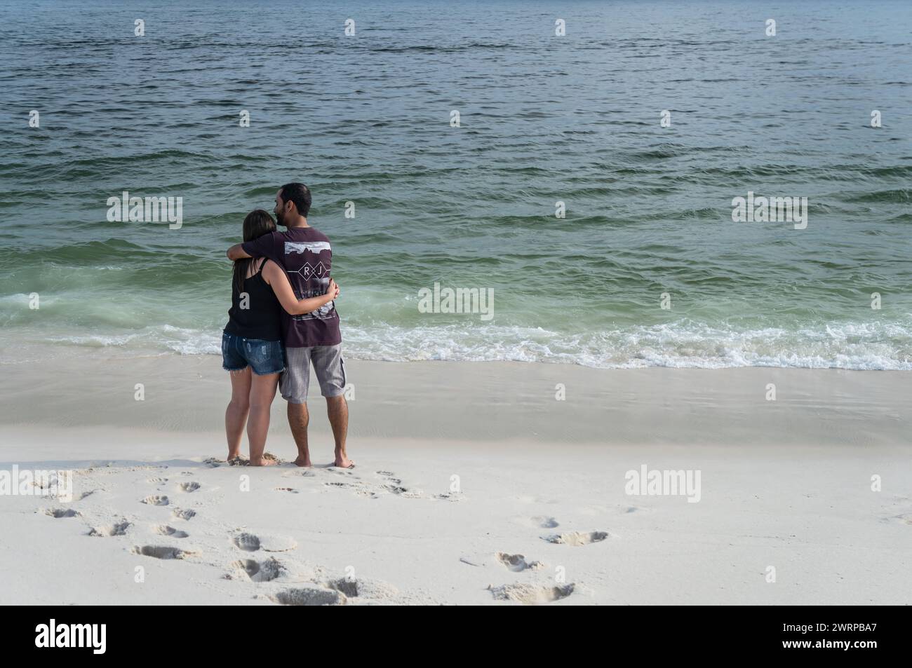Una coppia innamorata che si abbraccia mentre si trova sulle sabbie bianche della spiaggia di Praia Seca e guarda le acque dell'Oceano Atlantico nel pomeriggio estivo. Foto Stock