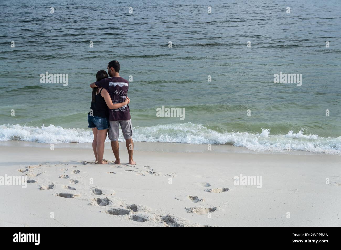 Una coppia innamorata che si abbraccia a vicenda in piedi sulle sabbie bianche della spiaggia di Praia Seca e guarda le acque dell'Oceano Atlantico nel pomeriggio estivo. Foto Stock