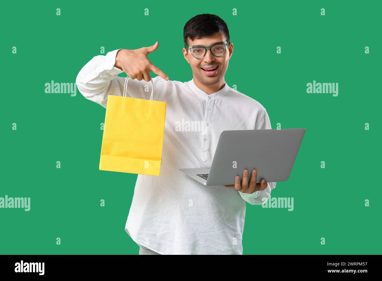 Bellissimo giovane con borsa della spesa e portatile su sfondo verde Foto Stock