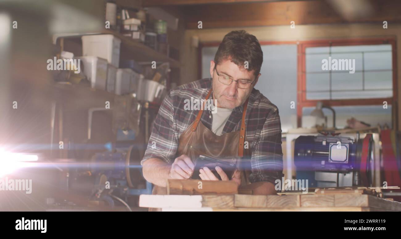 Immagine di una luce incandescente sull'uomo caucasico che usa un tablet in officina Foto Stock