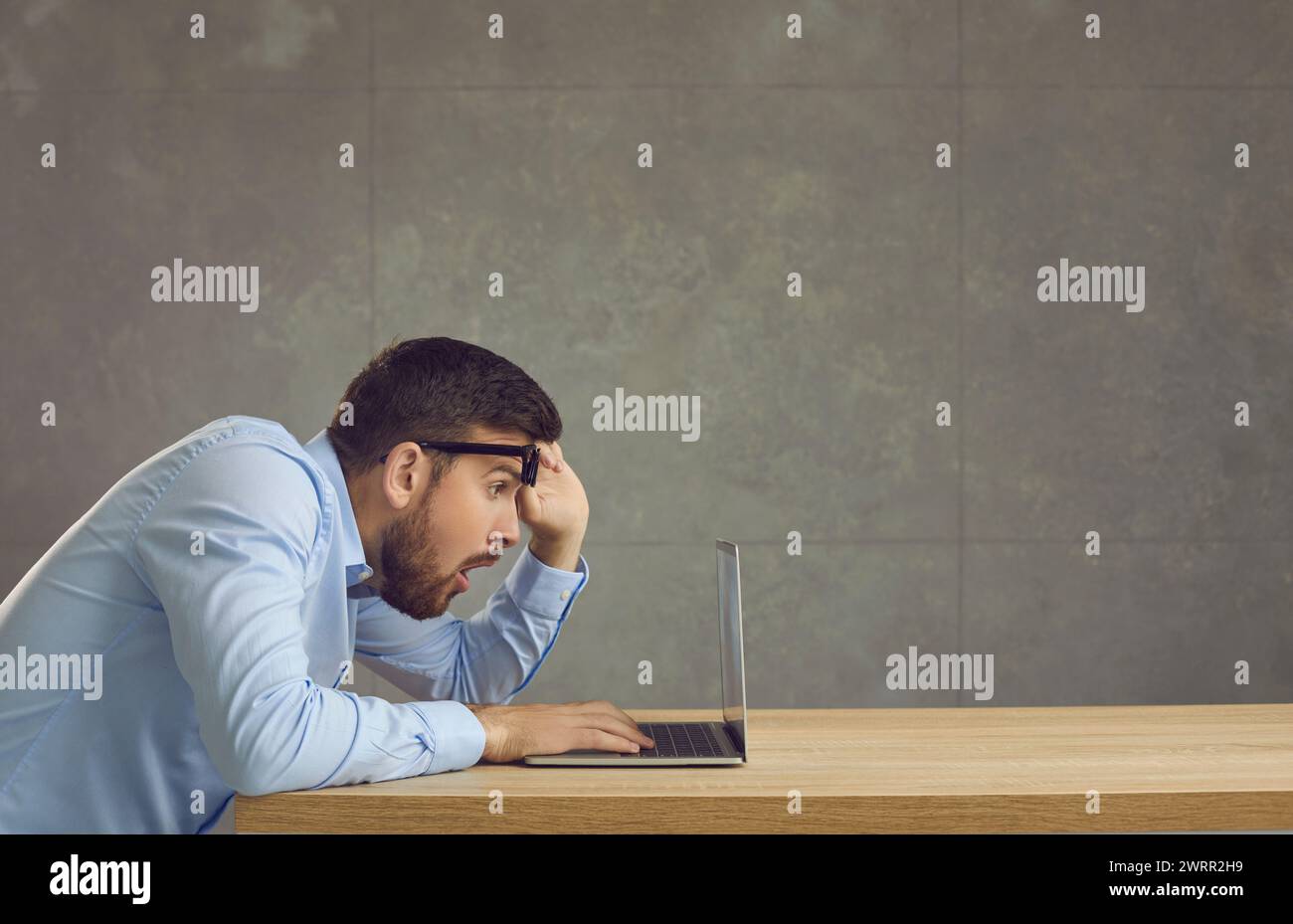 Un uomo stupito e scioccato con un'espressione confusa guarda lo schermo del notebook da sotto gli occhiali. Foto Stock