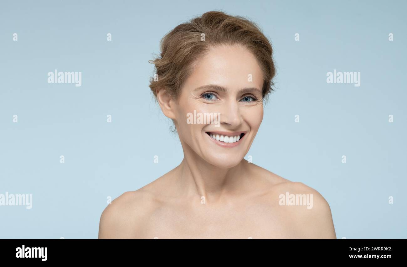 Ritratto di una donna di mezza età con una pelle radiosa e sana sullo sfondo blu. Concetto di cura della pelle Foto Stock