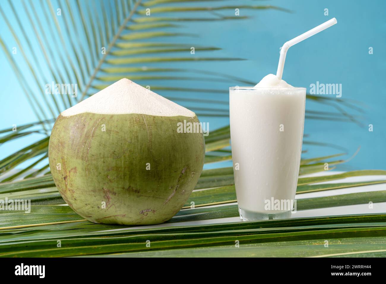 Un bicchiere di dolce profumo di cocco con acqua di cocco e sfondo blu. Foto Stock
