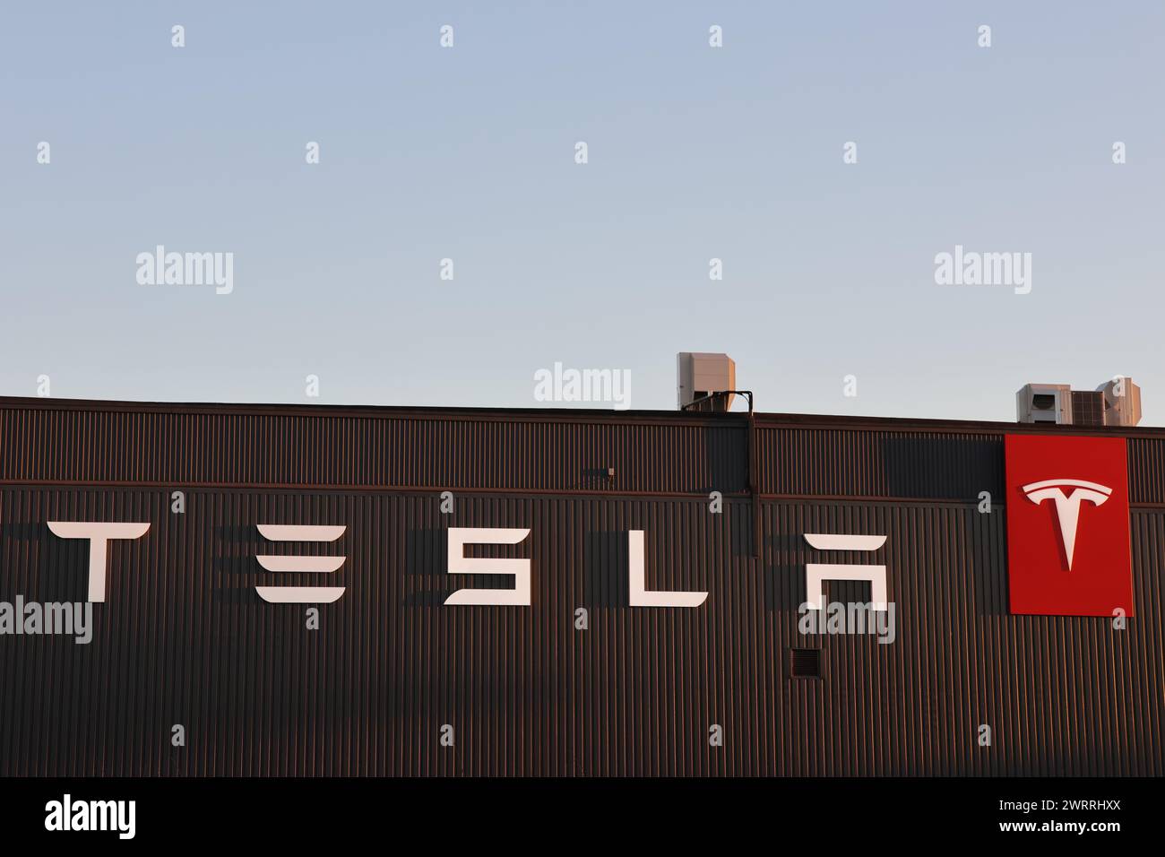 Il nuovo font Tesla in bianco su una parete marrone con logo Tesla rosso. Cielo blu nella parte superiore dell'immagine Foto Stock