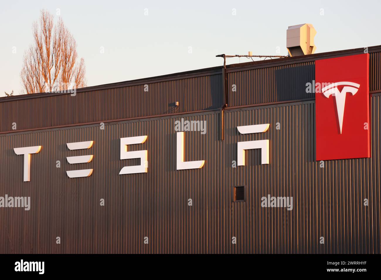 Il nuovo font Tesla in bianco su una parete marrone con logo Tesla rosso. Cielo blu nella parte superiore dell'immagine Foto Stock