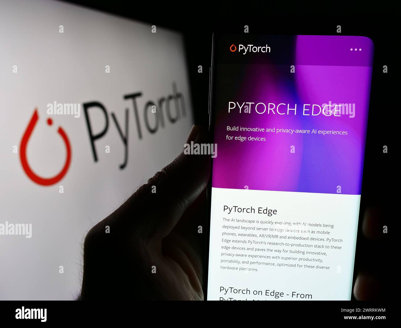 Persona che possiede lo smartphone con la pagina Web della libreria di apprendimento automatico PyTorch davanti al logo. Messa a fuoco al centro del display del telefono. Foto Stock