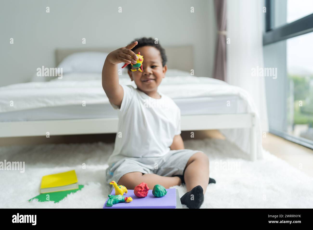 Simpatico bambino che realizza oggetti in plastica per terra Segui la tua immaginazione con un volto sorridente, luminoso e determinato. Foto Stock
