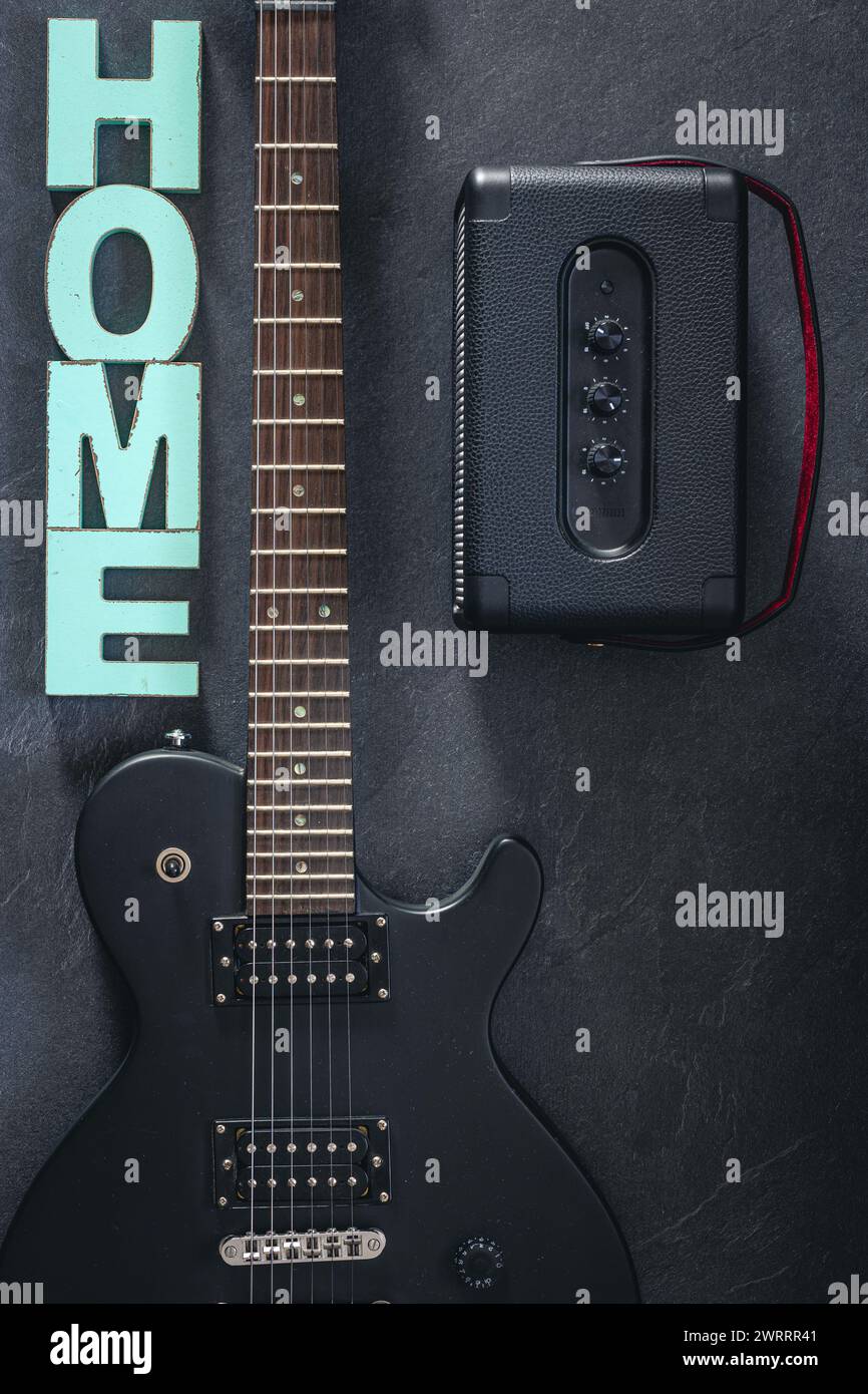 Chitarra elettrica e amplificatore su sfondo scuro con la parola decorativa Home. Foto Stock