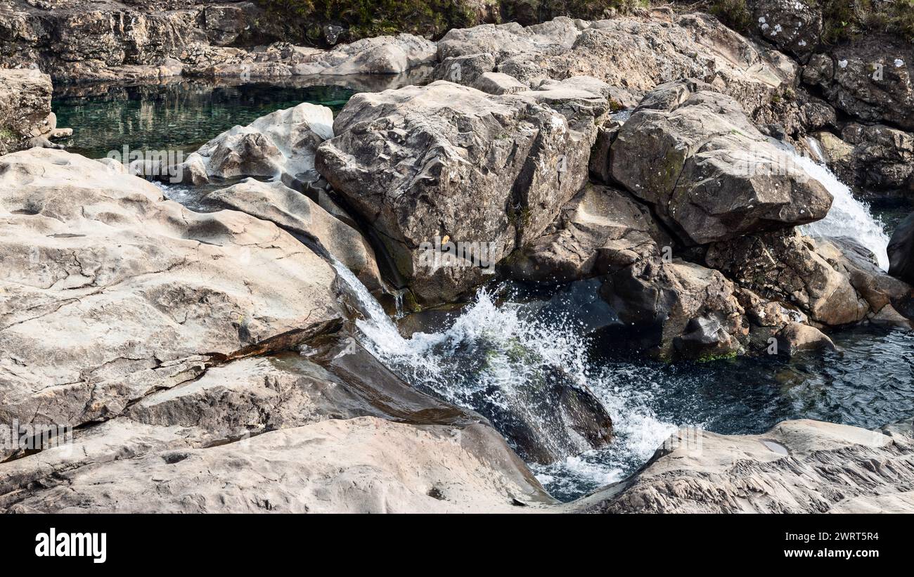 Cascate d'acqua cristallina sopra rocce aspre in tranquille piscine delle famose Fairy Pools dell'Isola di Skye, uno spettacolo naturale di meraviglia geologica Foto Stock