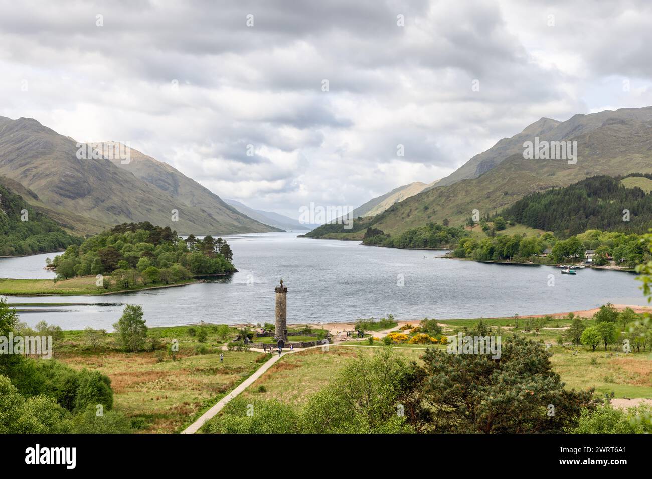 L'iconico monumento Glenfinnan si erge alto sul bordo dell'acqua, circondato dal lussureggiante paesaggio e dalle maestose montagne delle Highlands scozzesi unde Foto Stock