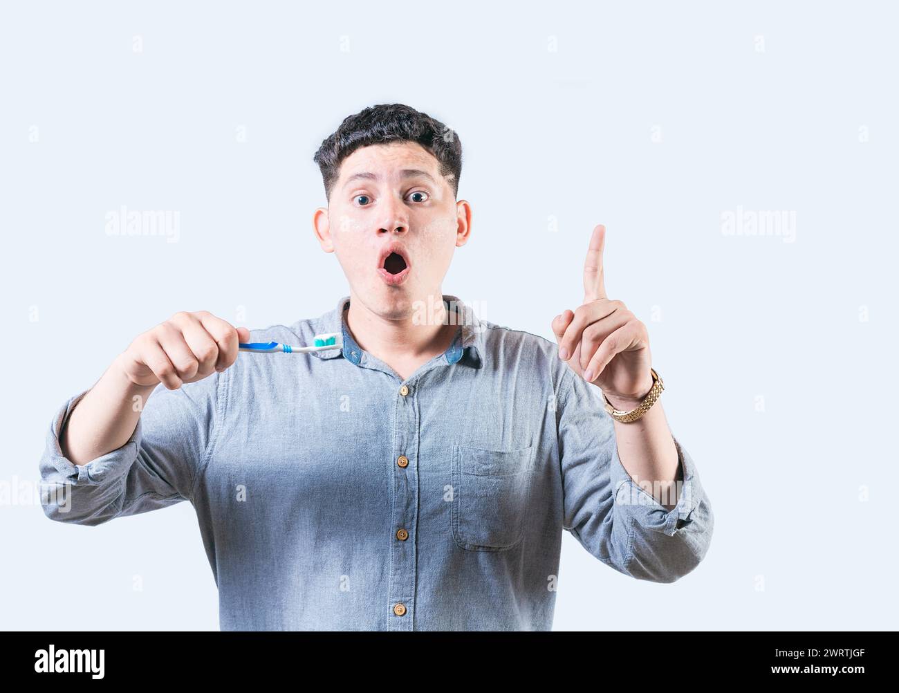 Un giovane sorpreso che tiene in mano uno spazzolino da denti che punta in alto isolato. Uomo stupito con lo spazzolino che punta la pubblicità Foto Stock