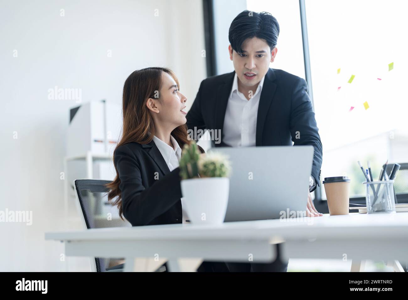 Gli uomini d'affari discutono insieme le iniziative aziendali visualizzando le informazioni attraverso un notebook in un moderno spazio di lavoro. Foto Stock