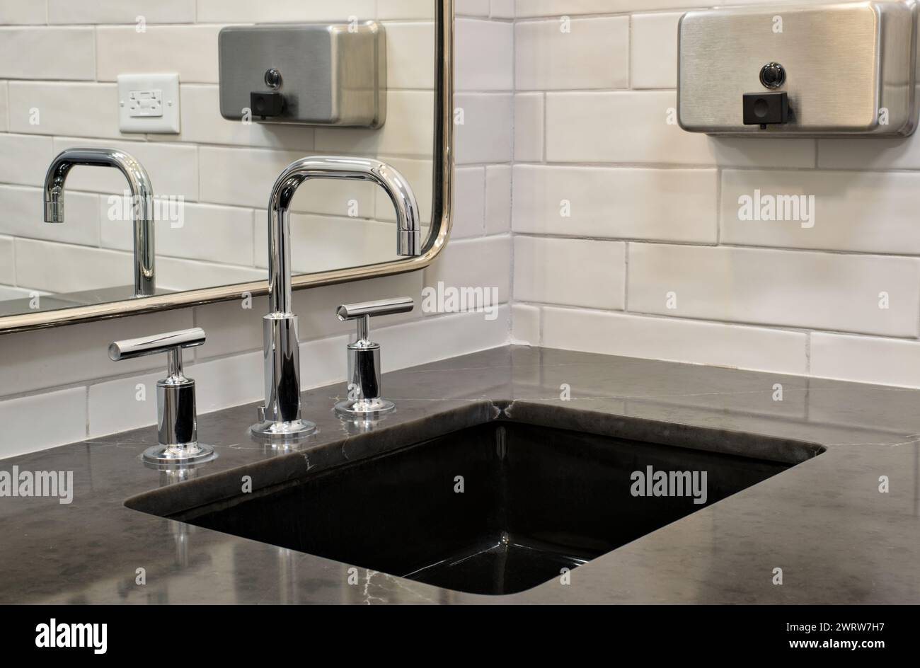 Lavandino del bagno con ripiano in marmo nero, specchio e dispenser di sapone, vista ad angolo basso. Foto Stock