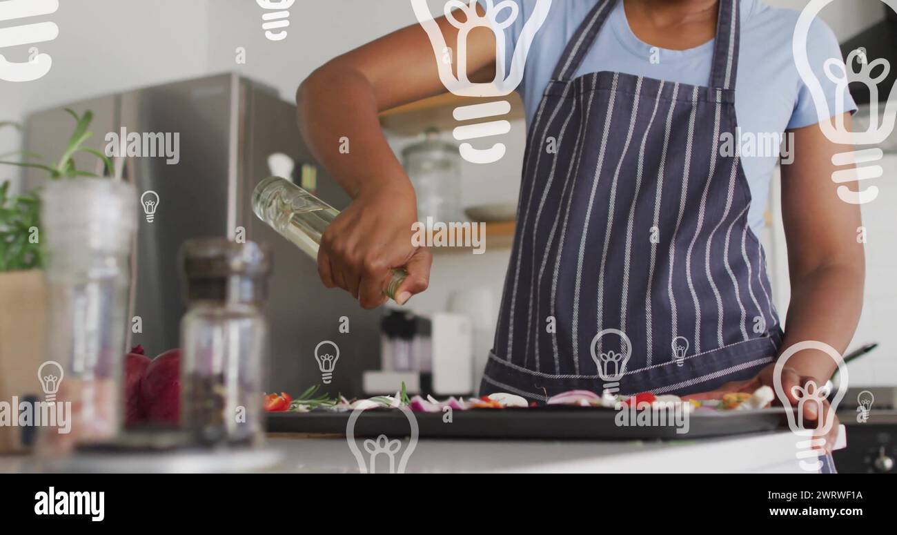 Immagine di lampadine sopra una donna afrcia americana che prepara il cibo in cucina Foto Stock