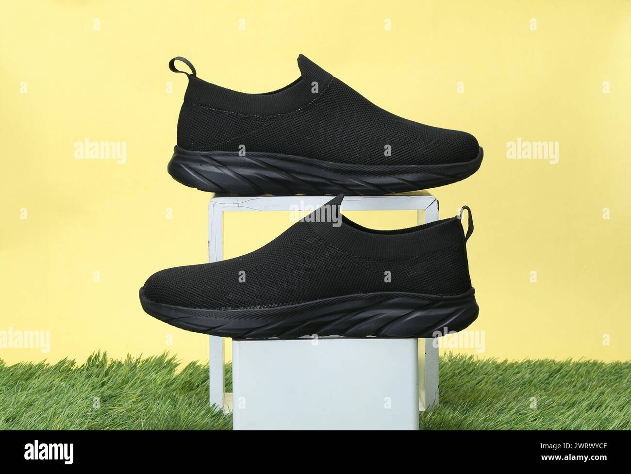 scarpe casual creative scattate su sfondo giallo con erba Foto Stock