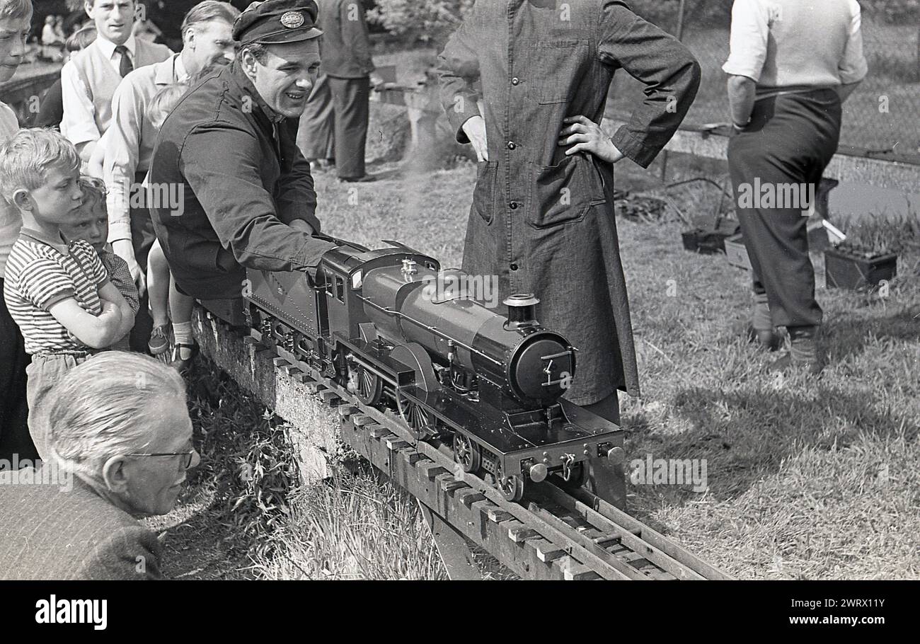 Anni '1970, storico, un autista di treni in tuta e cappello seduto su un treno a vapore in miniatura su un binario ferroviario sopraelevato, Inghilterra, Regno Unito. Foto Stock