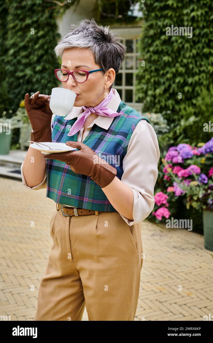 Bella donna matura e gioiosa che beve tè caldo a colazione nel giardino della sua casa in Inghilterra Foto Stock