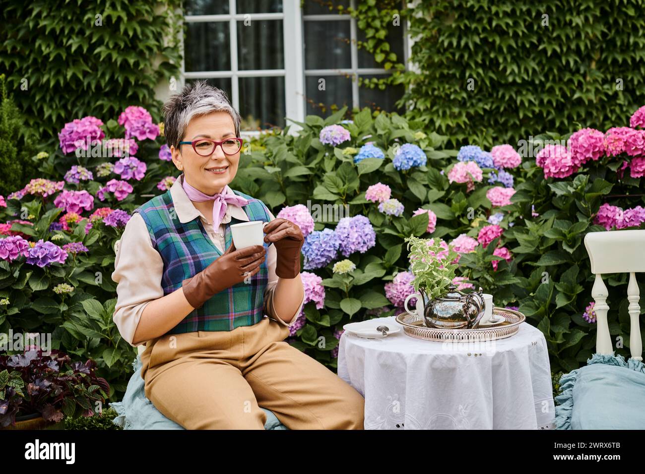 Bella donna matura che beve tè caldo a colazione nel giardino della sua casa in Inghilterra Foto Stock