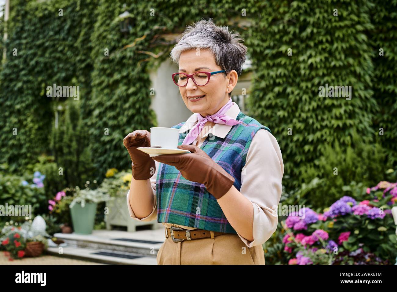 Bella donna matura e gioiosa che beve tè caldo a colazione nel giardino della sua casa in Inghilterra Foto Stock