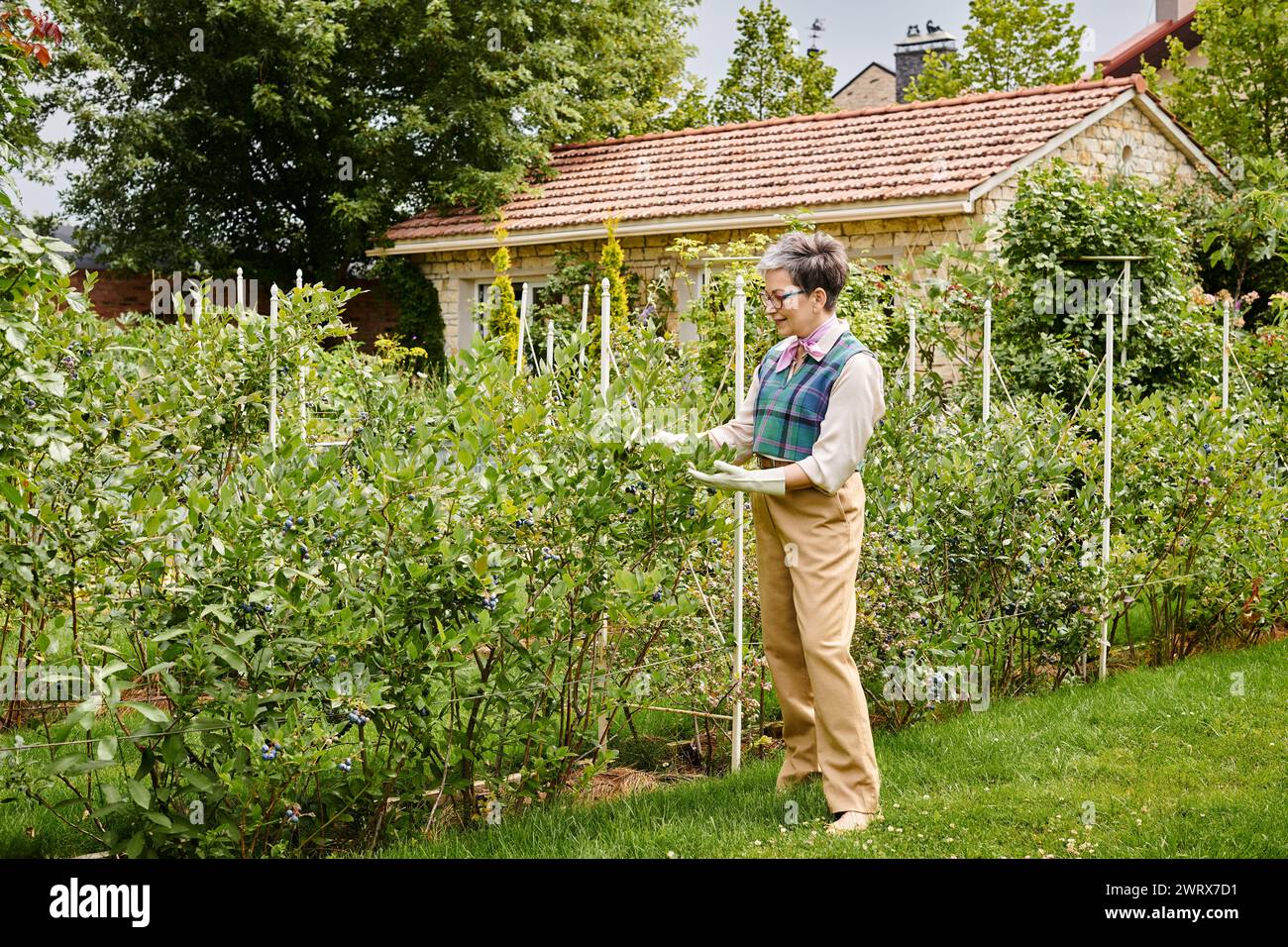 donna matura e sofisticata, gioiosa, con capelli corti e un abbigliamento elegante e vivace, che si prende cura delle sue piante Foto Stock