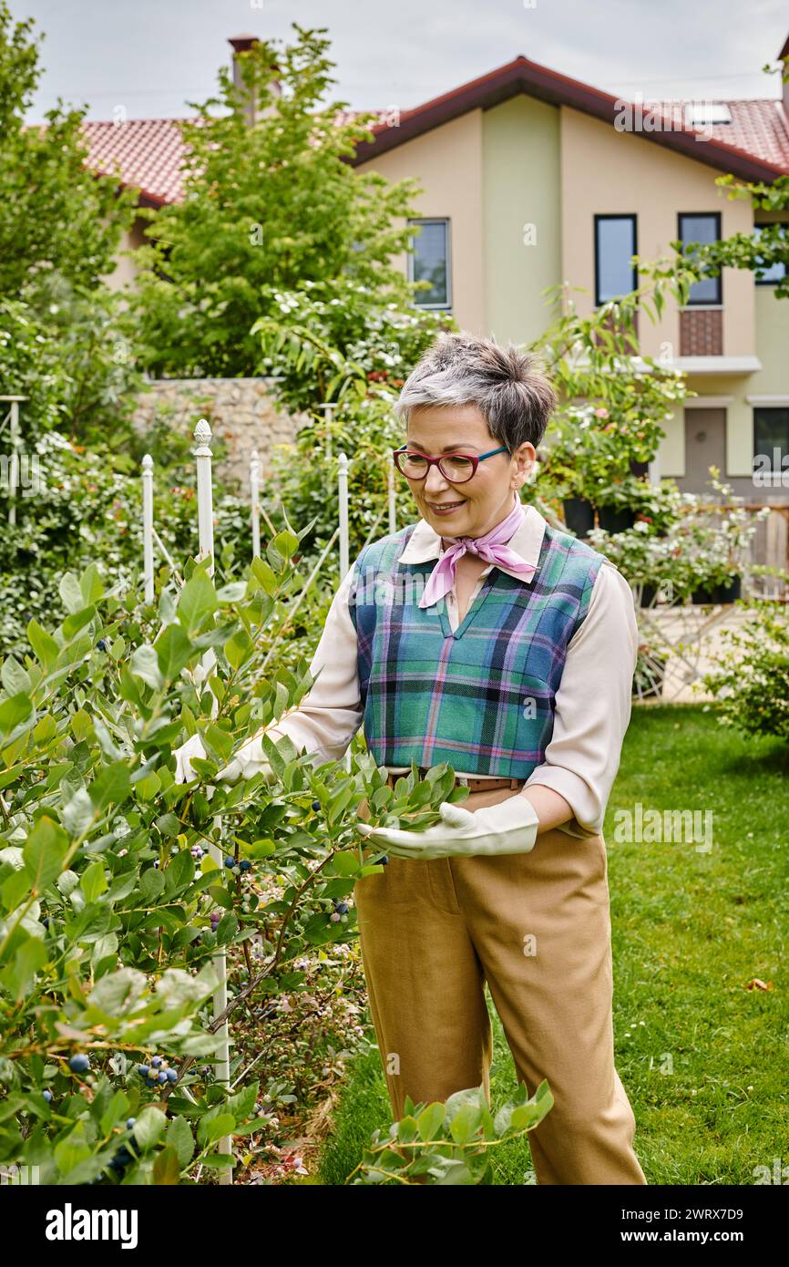 donna matura e sofisticata, gioiosa, con capelli corti e un abbigliamento elegante e vivace, che si prende cura delle sue piante Foto Stock
