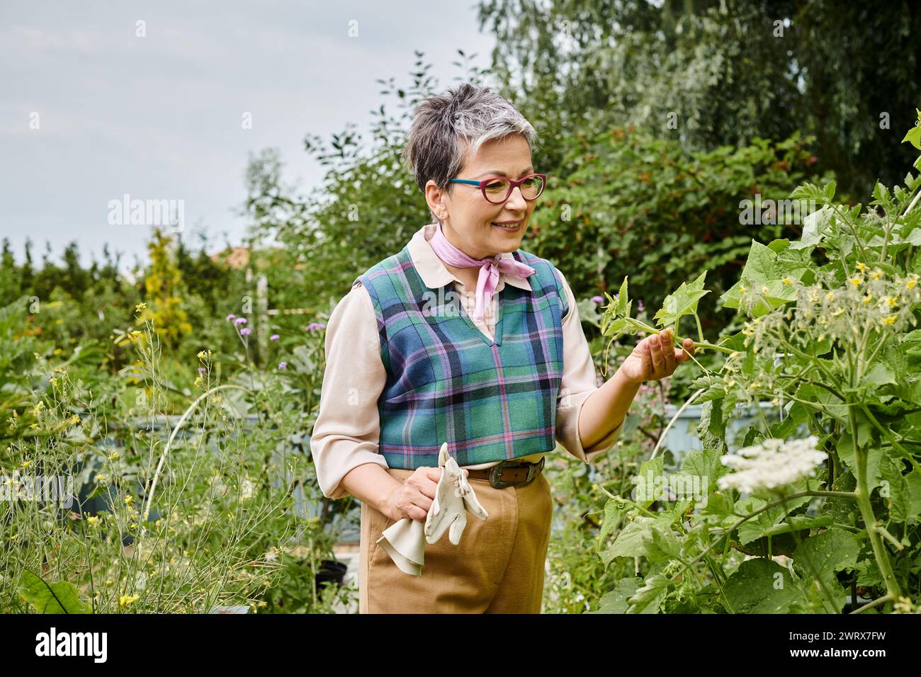 donna matura e sofisticata con capelli corti e un abbigliamento elegante e vivace che si prende cura delle sue piante Foto Stock