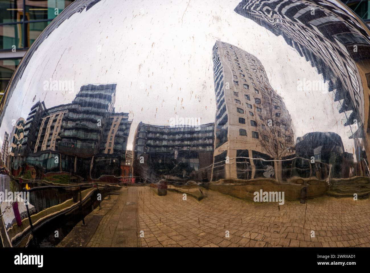 Un riflesso distorto di edifici alti sulla superficie di una scultura di palle d'acciaio, Leeds Dock, Yorkshire. Foto Stock