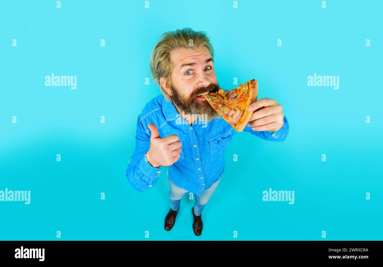 Pizzeria. Tempo della pizza. Uomo barbuto che mangia gustosa pizza mostrando il pollice in su. Cucina italiana. Pranzo o cena. Bel ragazzo in camicia di jeans che si diverte Foto Stock