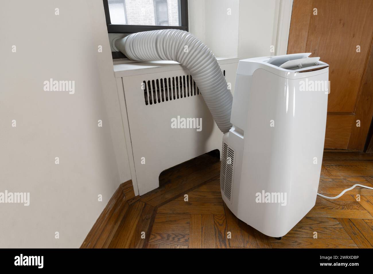 un impianto di aria condizionata portatile sul pavimento di un appartamento malandato con il condotto di ventilazione attaccato alla finestra Foto Stock