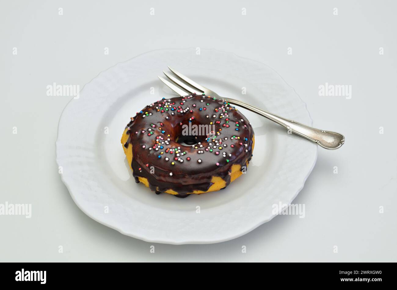 ciambella al cioccolato con spolverini di zucchero su piatto bianco con forchetta, primo piano. isolato su sfondo bianco Foto Stock