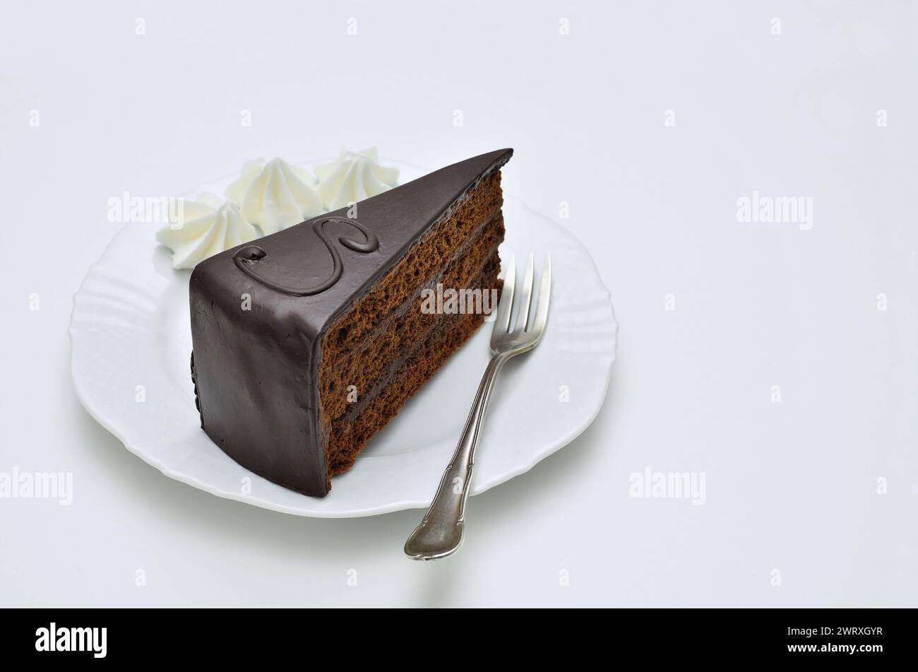 Un pezzo di torta Sacher con panna montata su piatto bianco, primo piano, isolato su sfondo bianco Foto Stock